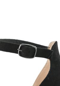 Scarpa con cinturino alla caviglia in camoscio nero, caratterizzata da una superficie testurizzata e una fibbia metallica argentata. Il tacco è slanciato per una silhouette classica.