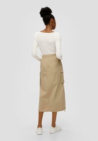 Beige enkellange rok met cargovakken en een elastische tailleband, gecombineerd met een witte langekleurige top. Gladde textuur, ontspannen pasvorm.