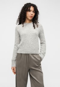 Gray, soft knit pullover sweater with a crew neck, ribbed cuffs, and a relaxed fit. Paired with light gray, loose-fitting trousers.