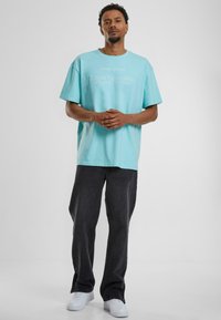 Mintgrønn, oversized bomulls t-skjorte med rund hals, med hvit tekstdesign, sammen med svarte vide jeans og hvite sneakers.