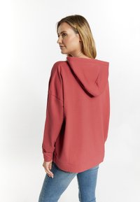 Felpa coral a vestibilità ampia con cappuccio e maniche lunghe. Tessuto morbido, orlo a coste e dettagli cuciti sulle spalle. Abbinata a jeans blu.