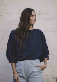 Navyblauwe, losvallende blouse met brede mouwen; gecombineerd met lichte, gestreepte, hoge taille broek. Gestructureerde stof, ontspannen ontwerp.