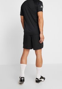 Svart atletisk t-shirt med kort ärm, som matchas med svarta shorts. Modellen har på sig vita strumpar och svarta fotbollsskor med vita detaljer.