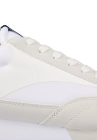 Weißer Sneaker mit einer Mischung aus glatten und strukturierten Materialien, gestickten Akzenten und geprägtem "GAP"-Logo an der Seite.