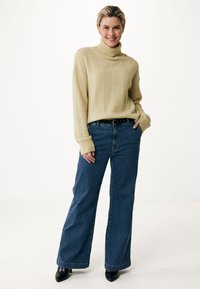 Maglione a collo alto di colore crema con un design a treccia, abbinato a jeans in denim blu a gamba larga e stivali neri con tacco.