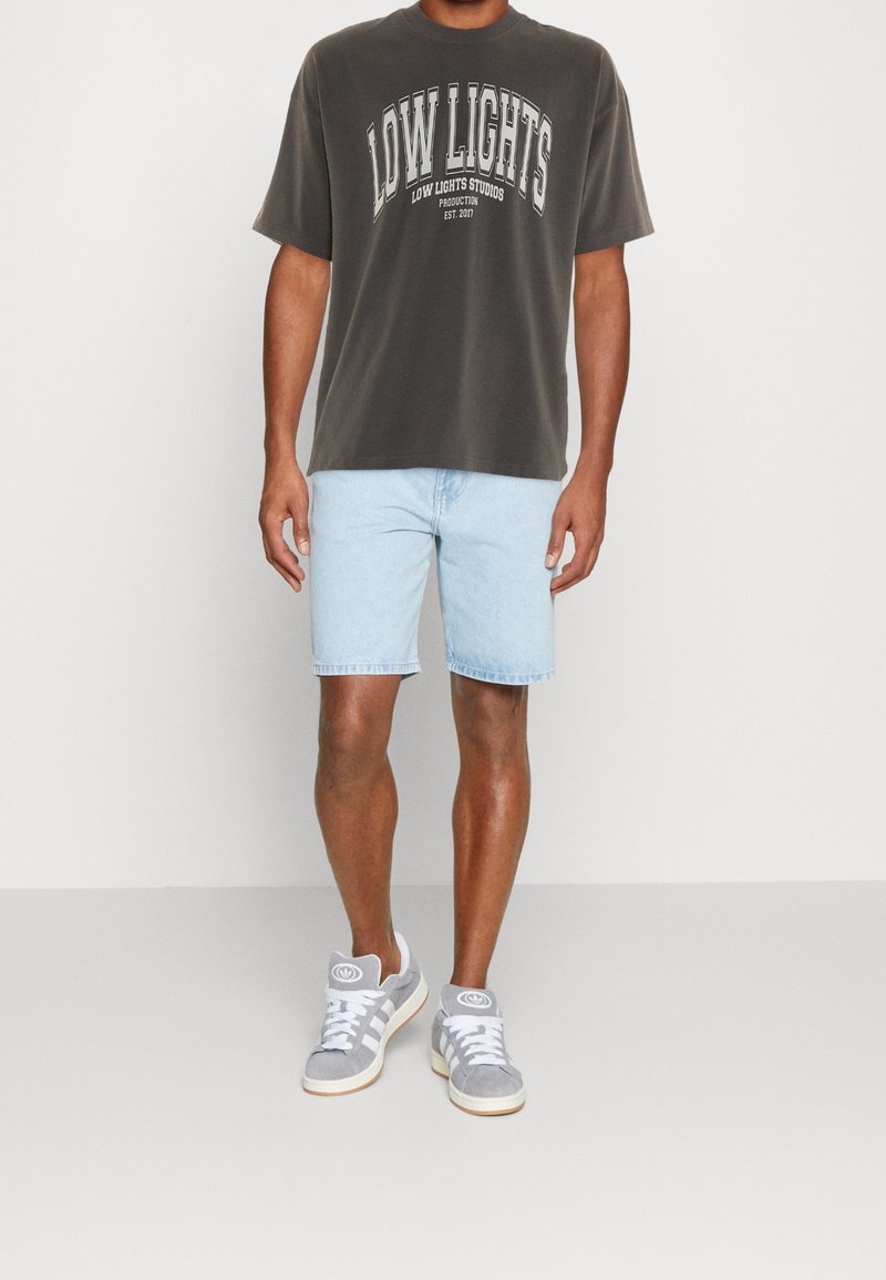 T-shirt surdimensionnée gris foncé avec un texte graphique blanc, short en denim bleu clair et baskets grises avec des lacets blancs et des détails de logo.