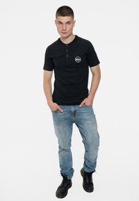 Black short-sleeve shirt with a round neckline and button detail, featuring a white Beatles logo. Worn with light blue jeans and black boots.