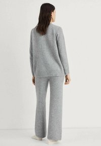 Maglione grigio a maglia e pantaloni a gamba larga abbinati realizzati in materiale morbido; entrambi presentano dettagli a costine sui polsini e sull'orlo.