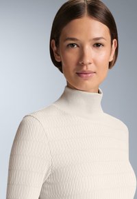 Beżowy prążkowany golf wykonany z miękkiego, teksturowanego materiału, o dopasowanym kroju i subtelnych liniach w tkaninie.