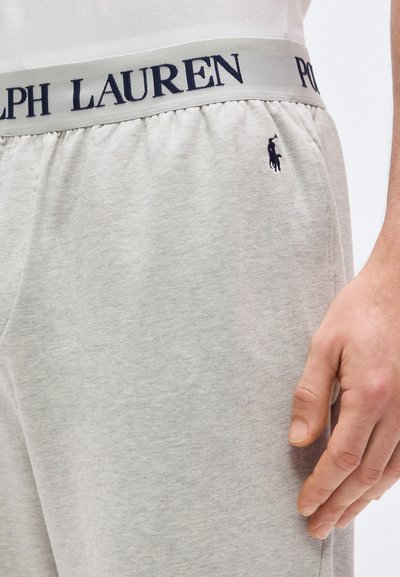 Κοντινό πλάνο ανοιχτόγριου παντελονιού φόρμας με γκρι ζώνη μέσης που φέρει το κείμενο "Ralph Lauren" και ένα μικρό μαύρο λογότυπο παίκτη πόλο στο ισχίο.
