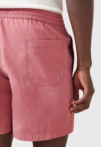 Lyserøde shorts lavet af letvægtsstof, med elastisk talje, stiklomme med øsken-detalje og en ren kant.