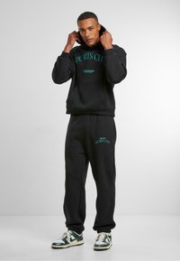 Svart bomullsgensar med hette og frontlomme, med turkise "SPORTS CLUB"-bokstaver. Matchende svarte sweatpants med lignende merke.