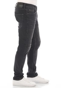 Jeans de mezclilla negra con un ajuste slim, que presentan un diseño tradicional de cinco bolsillos, un desvanecimiento sutil y una etiqueta en la cinturilla. Combinados con zapatillas blancas.