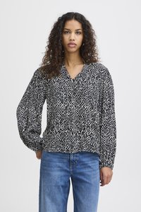 Blusa a righe bianco e nero con scollatura a V, maniche lunghe e vestibilità ampia, abbinata a jeans azzurri chiari. Tessuto morbido.