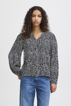 Blouse à motifs noir et blanc avec un décolleté en V, manches longues et coupe ample, associée à un jean bleu clair. Texture lisse.