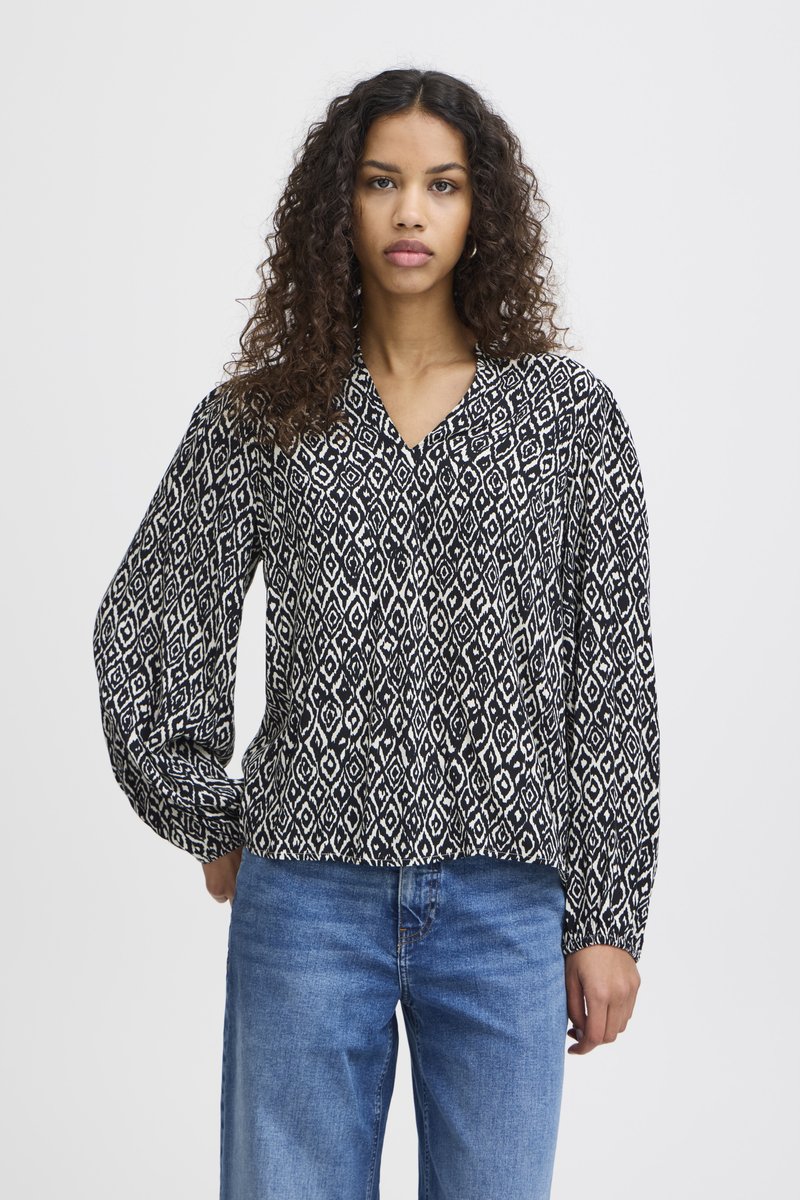 Blusa com padrão em preto e branco, com decote em V, mangas longas e um corte solto, combinada com jeans de tom azul claro. Textura suave.