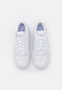 Bílé syntetické tenisky s perforovanou špičkou, plochými tkaničkami, polstrovaným límcem a logem Adidas na jazyku a patě. Mají hladký povrch.