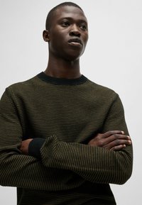 Maglione lavorato a maglia con un motivo a strisce testurizzato in verde scuro e giallo. Caratterizzato da un collo a giro e polsini a coste neri.