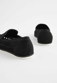 Black suede slip-on shoes with open design, textured sides, and white rubber soles. Features rounded back and minimal stitching details.