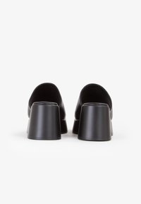 Scarpe nera in pelle con tacco quadrato, dalla texture liscia e bordi arrotondati, caratterizzate da un design a schiena bassa per una facile indossabilità.