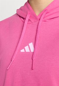 Roza kapucarjena majica z mehkimi vlakni, z vrvicami in belim Adidasovim logotipom na prsih.