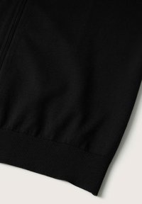 Tela de sudadera de algodón negro con textura suave, que presenta un dobladillo acanalado y costuras laterales, mostrando un diseño simple y casual.