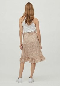 Bloemige wikkelrok in licht perzik, met kleine veelkleurige bloemen. Rimpelzoom, gemaakt van lichte stof, gecombineerd met een witte tanktop en sneakers.