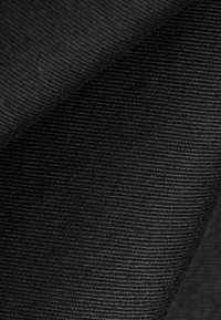 Primer plano de tela de pana negra que muestra su patrón texturizado de estrías y un pliegue diagonal.