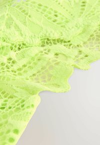 Tissu en dentelle de couleur vert clair vif, avec des motifs intricats, un tissage ajouré et des bords festonnés. Texture douce avec une apparence délicate.