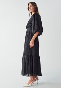 Black mid-length dress with puffed sleeves, textured fabric, and a tied waist. Paired with white pointed heels for contrast.