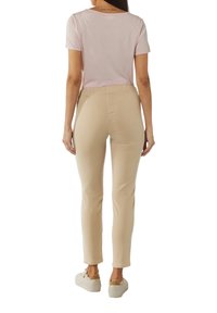 Helles rosa T-Shirt mit kurzen Ärmeln, kombiniert mit beigen Slim-Fit-Hosen. Die Hosen haben eine glatte Textur und einen elastischen Bund, abgerundet mit weißen Sneakers.