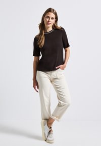 Black short-sleeved top with a round neckline, paired with cream-colored cropped pants and light-colored sneakers. Smooth fabric, minimal design.