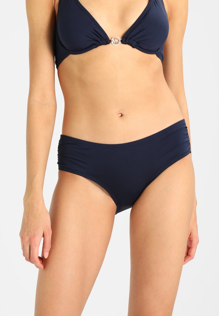 Sötétkék bikini, háromszög alakú toppal, középen csavarral és ezüst kör alakú logóval, párosítva ruházott alsó résszel.
