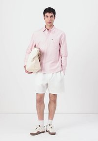 Lys rosa stripete skjorte med knapper, hvite teksturerte shorts og beige veske. Hvite sneakers med brune detaljer. Enkel, moderne design.