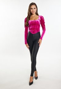 Fuchsia velours langærmet bluse med firkantet halsudskæring og draperede skuldre, parret med sorte højtaljede skinny bukser og sorte hæle.