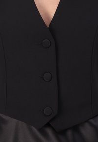 Zwarte mouwloze vest met een diepe V-hals, voorzien van drie ronde knopen en een gestructureerde vorm, gemaakt van een gladde, matte stof.