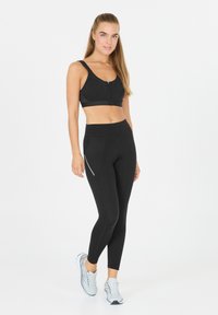 Svart sportbh med framsida dragkedja, i kombination med svarta leggings med sidofickor och silverdetaljer. Slät, elastisk tyg; figurnära design.