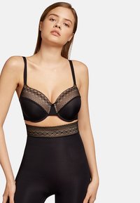 Reggiseno in pizzo nero con coppe imbottite e spalline regolabili, caratterizzato da un sottile strato di pizzo trasparente e bordi ondulati; abbinato a leggings neri a vita alta.