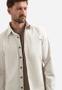 Licht beige button-up shirt met twee voorzakken. Zachte stof en een relaxed fit, met een casual kraag en zwarte knopen.