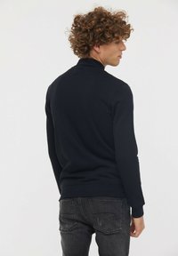 Pull en tricot noir avec un col montant, des manches longues et des bords côtelés aux poignets et en bas. Texture lisse, design ajusté et détails minimalistes.