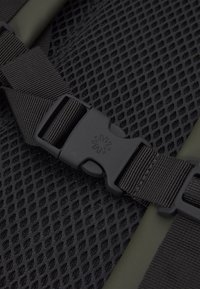 Tissu en maille noir avec un fond vert olive, comportant une boucle en plastique noir robuste et des sangles en sangle réglables.