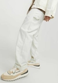 White cotton wide-leg pants with a textured finish, featuring side pockets. Paired with beige and white athletic shoes.