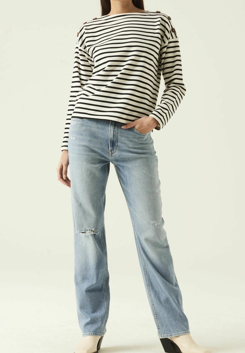 Randig långärmad topp i krämfärg och svart, kombinera med ljusblå slitna jeans. Signifikanta knappdetaljer på axlarna och vid byxpassform.