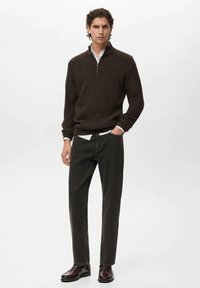 Maglione a coste marrone scuro con collo a mezza zip, abbinato a pantaloni neri e scarpe lucide scure. Camicia bianca visibile al colletto.