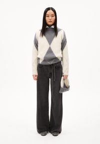 Grauer und elfenbeinfarbener Rautenmuster-Pullover, lockere schwarze Denim-Hose, gemusterte Schuhe und hält einen passenden grau-elfenbeinfarbenen Hut. Einfaches, lässiges Design.