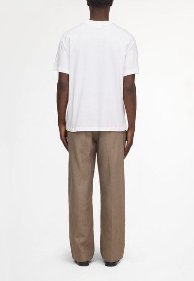 Man facing away wearing a plain white short-sleeve shirt and loose light brown pants against a white background.