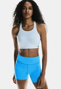Top sportivo bianco con spalline larghe abbinato a pantaloni shorts high-waisted di un blu brillante. Entrambi i capi presentano un tessuto liscio e elasticizzato.