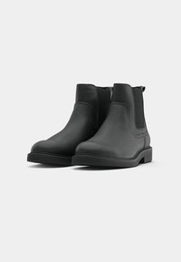 Botine Chelsea negre din piele, cu panouri laterale elastice, vârf rotund și talpă din cauciuc texturat. Design simplu și clasic.
