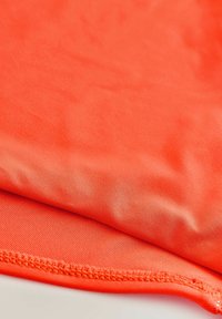 Detail stehu na jasne oranžovej látke, zobrazujúci hladkú textúru a jemné diagonálne rebrovanie.