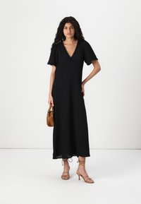 Black, mid-length dress with a v-neckline and short puff sleeves, featuring lace trim. Paired with tan high-heeled sandals and a brown handbag.